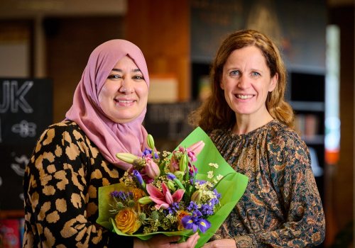Yamina Ayada en Mirjam van Rijn kijken lachend in de camera met bos bloemen in de hand