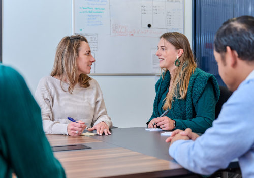 Vier collega's overleggen aan tafel en maken notities 