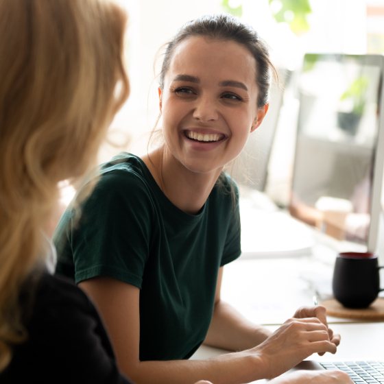 Jonge vrouw voor laptop lacht naar collega